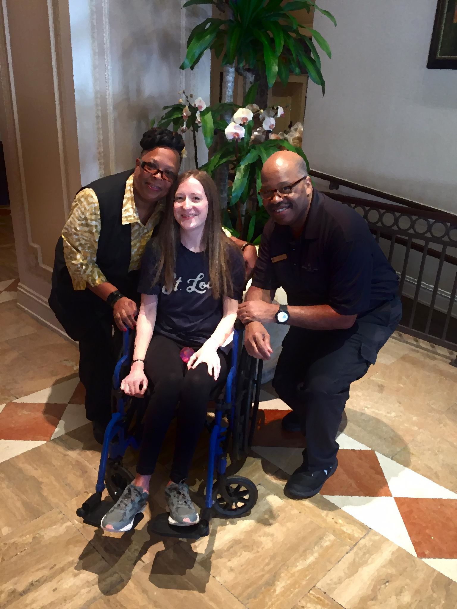 Miss Brenda and James posing next to Kerry (the author of this post) after one of her surgeries. Kerry is sitting in a wheelchair wearing a St. Louis t-shirt. All three are smiling.